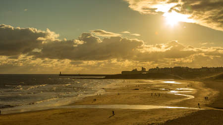 People taking a walk on Tynemouth's Longsands beach during Lockdown on a cloudy and rainy day, in the north east of Englandの写真素材