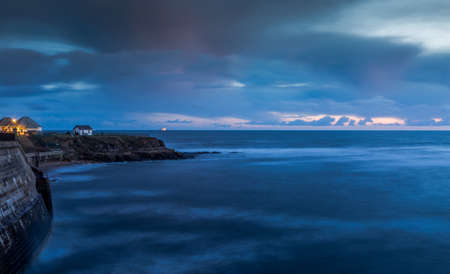 A white house on the cliffs in Cullercoats during Blue hour with clouds over-headの写真素材