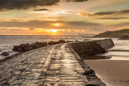 Sunrise at a chilly Cullercoats Bay in the north east of England, with Tynemouth Pier and the lighthouse in the distance.の写真素材