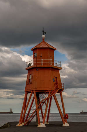 The old, red, wooden Herd Groyne Lighthouse in South Shields, stands out against the dramatic, cloudy skyの写真素材