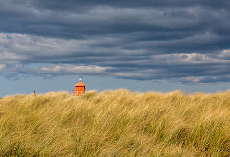 The old, red, wooden Herd Groyne Lighthouse in South Shields, stands out against the dramatic, cloudy skyの写真素材