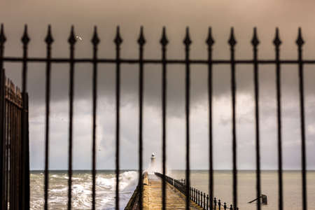 Tynemouth Pier and the Lighthouse through the metal railings on a cloudy dayの写真素材