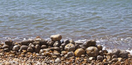 some pebbles stacked up on a pebbly beach close to the waters edgeの写真素材