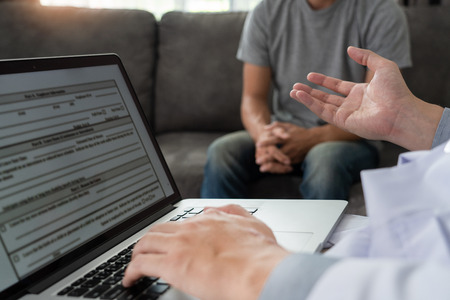 Geriatric doctor or geriatrician concept, Doctor visiting with patient in room and hearing serious disease diagnose writing on clipboard while consulting a man at homeの写真素材