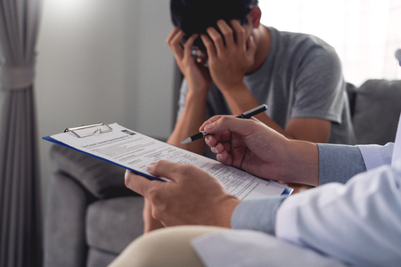 Geriatric doctor or geriatrician concept, Doctor visiting with patient in room and hearing serious disease diagnose writing on clipboard while consulting a man at homeの写真素材