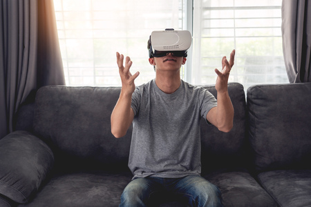 a cheerful man sitting on couch and wearing 3D virtual reality glasses