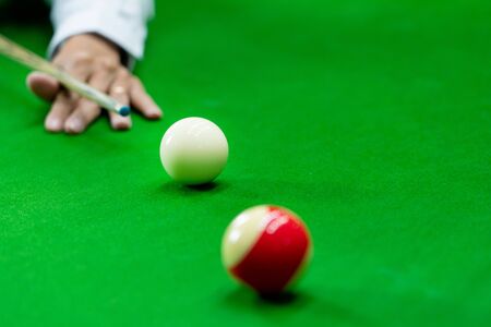 Man's hand and Cue arm playing snooker game or preparing aiming to shoot pool balls on a green...