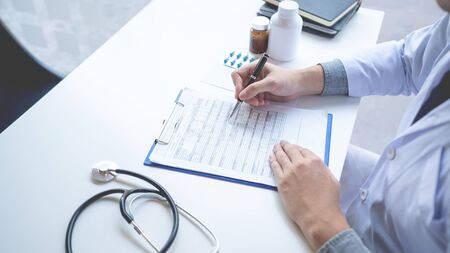 Doctor reading on a document report and writing on paperwork and searching treatment information at office, Medical healthcare conceptの写真素材