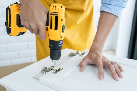 close up man holding cordless screwdriver machine and screws lie for screwing a screw assembling furniture at homeの写真素材