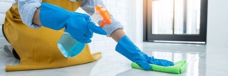 Housekeeper maid wearing rubber gloves with cloth cleaning or applying floor care and cleaners at...