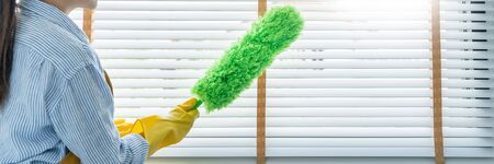 Young female spring cleaning house interior holding a duster for wiping dust dusting furniture at...