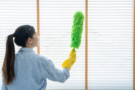 Young female spring cleaning house interior holding a duster for wiping dust dusting furniture at homeの写真素材