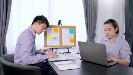 Young pensive asian man working late concentrated and serious in front of computer at night in dark...