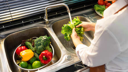 Woman hands washing Vegetables for Preparation of vegan salad on the worktop near to sink in a...