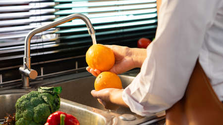 Woman hands washing Vegetables for Preparation of vegan salad on the worktop near to sink in a modern kitchen, Homemade healthy food conceptの写真素材