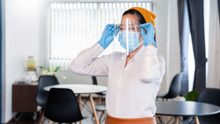 attractive asian waitress wear face mask and face shield to protection epidemic virus outbreak coronavirus disease COVID-19 in her restaurant, new normal conceptの写真素材