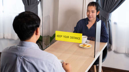 Asian couple sitting separated in restaurant eating food with table shield plastic partition to protect infection from coronavirus (covid-19), Social distancing rules in practice after lockdownの写真素材