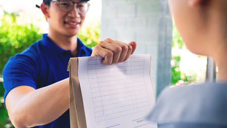 Asian deliver man in uniform handling bag of food vegetables and greens to customer at door home,...