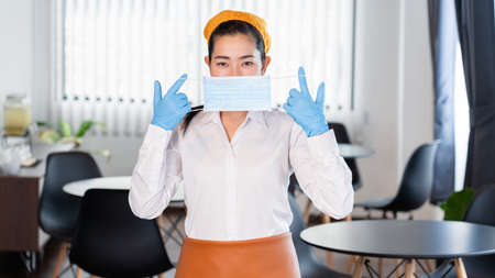 attractive asian waitress wear face mask to protection epidemic virus outbreak coronavirus disease COVID-19 in her restaurant, new normal conceptの写真素材