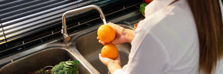 Woman hands washing Vegetables for Preparation of vegan salad on the worktop near to sink in a modern kitchen, Homemade healthy food conceptの写真素材