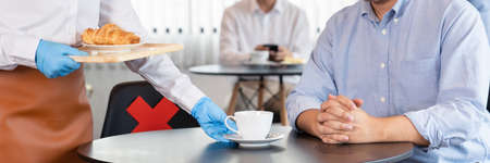 waitress wearing protective face mask and gloves for outbreak prevention Coronavirus (Covid-19) serves coffee in a restaurant, new normal and Social distancing conceptの写真素材