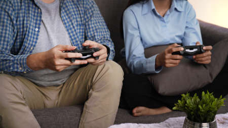 Excited funny young couple playing video games holding game controller sitting on sofa having fun...