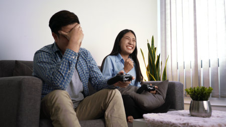 Excited funny young couple playing video games holding game controller sitting on sofa having fun...