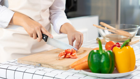 young Asian woman is preparing healthy food vegetable salad by Cutting tomato for ingredients on cutting board on light kitchen, Cooking At Home and healthy food conceptの写真素材