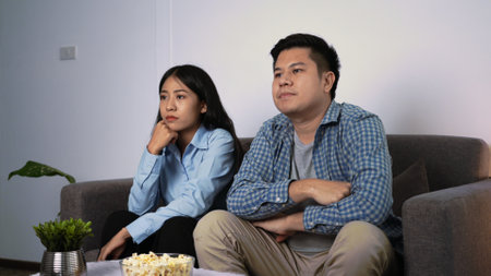 Happy young asian couple laying sofa in their cozy living room watching movie on television and...