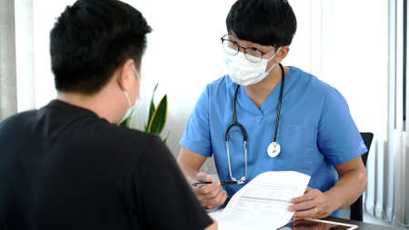Asian man doctor wear protection face mask and flu outbreak is taking care examining sick patient in hospital.の写真素材