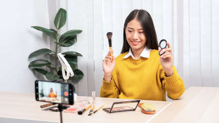 Asian woman present beauty cosmetic product and broadcast live video to social network by internet at home, beauty blogger conceptの写真素材