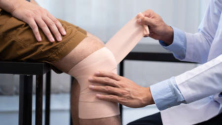 Medical concept a male doctor putting a bandage on knee's male patient after his accident.の写真素材