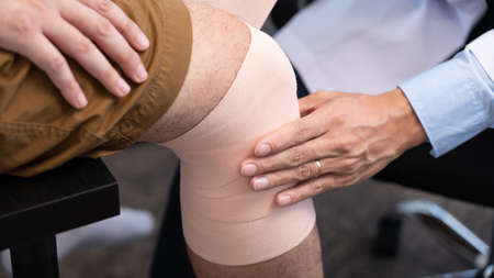 Medical concept a male doctor putting a bandage on knee's male patient after his accident.