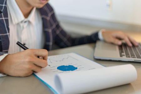 Business partners concept a young businessman using a laptop revising annual sales summary.