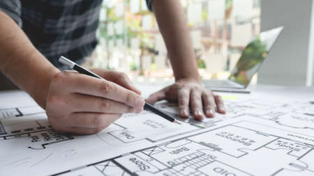A male architect measuring and marking the scale ratio of sizes of a complicated blueprint.の写真素材