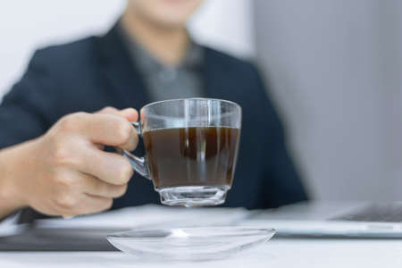 Business partners concept a young male entrepreneur holding a cup of black coffee sitting with a...
