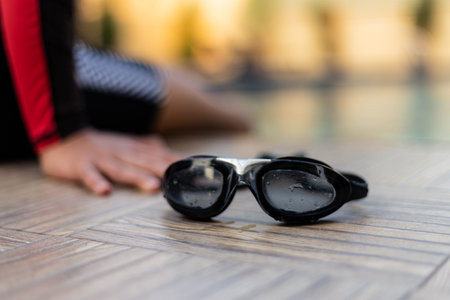 Sports and recreation concept black swimming goggles placed at a swimming pool with a boy wearing a swimming suit.の写真素材