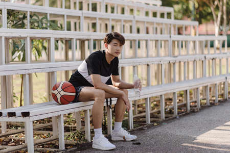 Sports and recreation concept a young male basketball player sitting on a grandstand on the border of the sports court.の写真素材