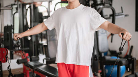 Training gym concept a male teenager using a gym equipment pulling his both muscular arms against...