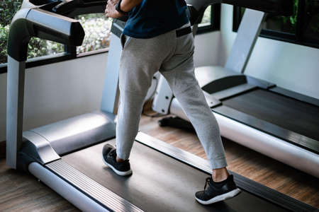 Training gym concept a male teenager wearing long pants and black trainers walking on a treadmill for cardio workout.の写真素材