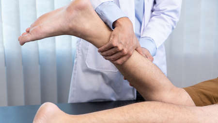 Medical concept a male doctor diagnosing a male patient's leg by pressing his leg because of playing...