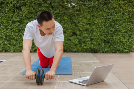 Training gym concept a young male adult doing exercise while going on social media with his laptop during a pandemic.の写真素材