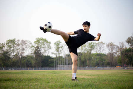 Sports and recreation concept a male soccer player wearing black t-shirt and pants practicing kicking the ball in the grassy field.の写真素材