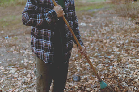 Gardening concept a male gardener using a coconut-leaf broom gathering the dry fallen leaves for cleaning the area.の写真素材