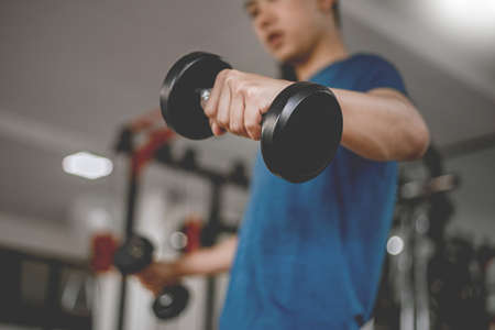 Training gym concept a young adult using his muscular strong arm lifting a dumbbell upward and downward in the gym.の写真素材