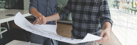 two male colleagues collaborating an architecture project about roomsâ position in a blueprint.の写真素材