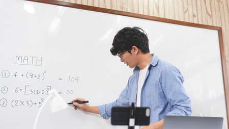 Educational concept A young smart male teacher looking at webcam and teaching online lesson by video conference call on a computer during the coronavirus outbreak.の写真素材