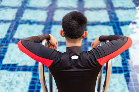 Sports and recreation concept a well-built boy sitting on the border of a blue-sky swimming pool enjoying the sunlight and lively weather.の写真素材