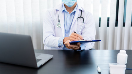 Medical concept a male doctor wearing a mask writing prescription to patient for recovering from Coronavirus (COVID-19) at his modern clinic.の写真素材