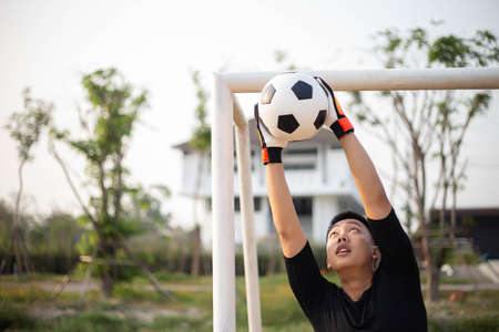 Sports and recreation concept a young male goalkeeper using his both hands catching the ball as preventing the opposing team from scoring.の写真素材